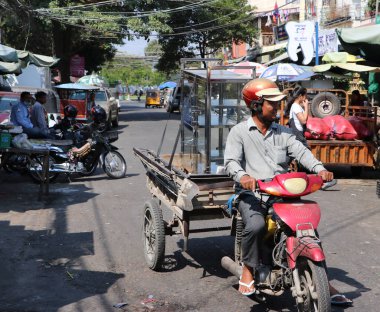 Phnom Penh, Kamboçya, 30 Ocak 2019: Kamboçyalı erkek sokakta teslim edilmek üzere cam dolaplar taşıyan üç tekerlekli motosiklete biniyor.
