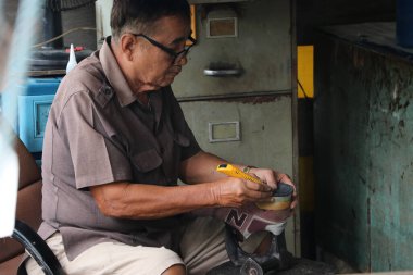 Lat Lum Kaeo, Pathum Thani, Tayland, Sep 9, 2019: Ayakkabı tamirinde uzman olan yaşlı bir adam ayakkabılarını tamir ediyor..