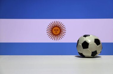 Beyaz zeminde beyaz, açık mavi ve Arjantin bayrağı arkaplanının güneşi arasında küçük bir futbol topu. Spor konsepti.