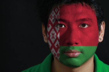 Yüzünde Belarus bayrağı olan bir adamın portresi siyah zemin üzerine boyanmış, 2: 1 oranında kırmızı üzerine yeşil, beyaz dikey çizgili kırmızı süslemeli bir desen..
