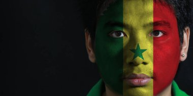 Yüzünde Senegal bayrağı olan bir adamın portresi siyah zemin üzerinde, yeşil sarı ve kırmızı, merkezinde yeşil bir yıldızla yüklenmiş..