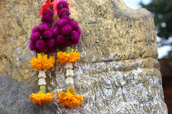 Flower garland of purple globe amaranth with yellow marigold and crown flower hanging on the rock.