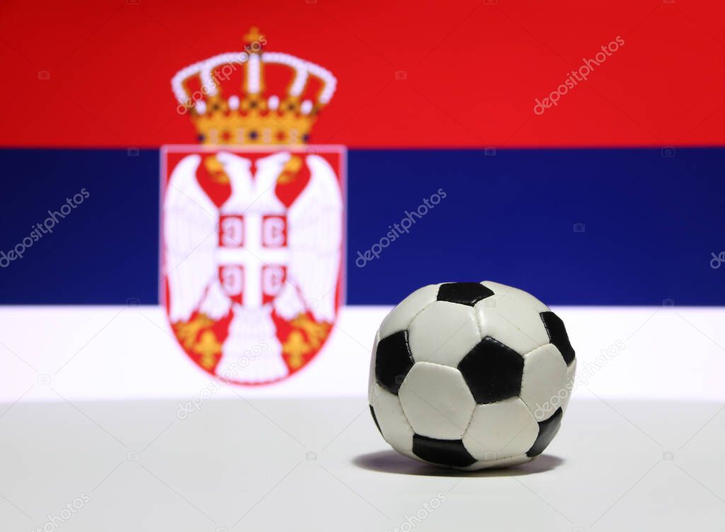 Small football on the white floor with white blue and red color, out focus eagle and crown picture of Serbian nation flag background. The concept of sport.
