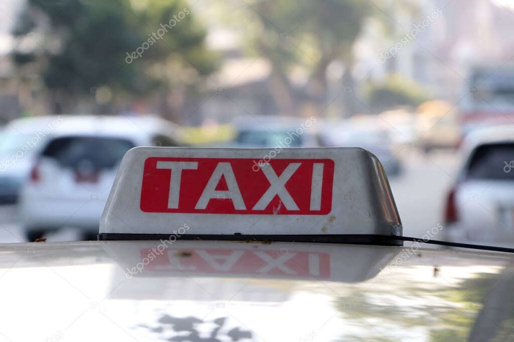 Taxi light sign or cab sign in drab white and red color with white text on the car roof at the street blurred background, Myanmar.