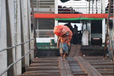 Yangon, Myanmar, 24 Şubat 2019: Myanmese işçisi gemiden hindistan cevizi kabuğu taşıyor ve Yangon Nehri 'ndeki liman köprüsünü geçiyor.
