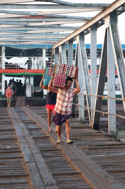Yangon, Myanmar, 24 Şubat 2019: İki Myanmalı işçi gemiden ördek yumurtaları taşıyor ve Yangon Nehri 'ndeki liman köprüsünü yürüyerek geçiyorlar..