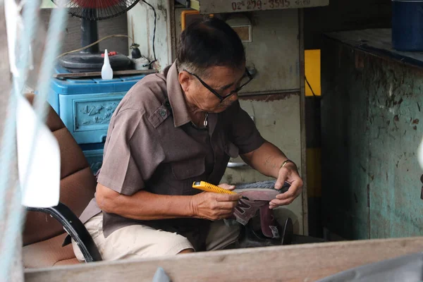Lat Lum Kaeo, Pathum Thani, Tayland, Sep 9, 2019: Ayakkabı tamirinde uzman olan yaşlı bir adam ayakkabılarını tamir ediyor..