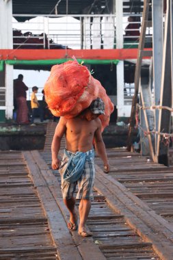 Yangon, Myanmar, 24 Şubat 2019: Myanmese işçisi gemiden hindistan cevizi kabuğu taşıyor ve Yangon Nehri 'ndeki liman köprüsünü geçiyor.