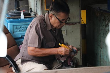 Lat Lum Kaeo, Pathum Thani, Tayland, Sep 9, 2019: Ayakkabı tamirinde uzman olan yaşlı bir adam ayakkabılarını tamir ediyor..