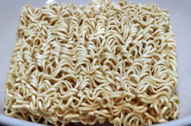 Çiğ erişte kareleri beyaz kasede yakın çekim şeklinde. Önceden pişirilmiş ve kurutulmuş erişte bloğunda, aroma tozu ve / veya baharat yağı ile birlikte..