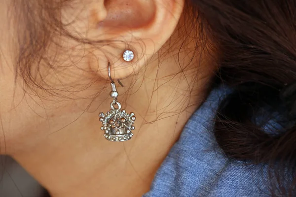 Crown shape of metal earring with diamond earring on the ear of long hair woman.