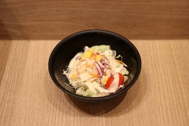 Ahşap zemindeki küçük siyah kasede sebze salatası. Çiğ sebze karışımından oluşan bir yemektir..