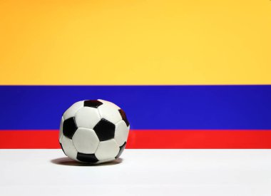 Beyaz zeminde küçük bir futbol topu ve sarı mavi ve kırmızı arka planda Kolombiya bayrağı. Spor konsepti