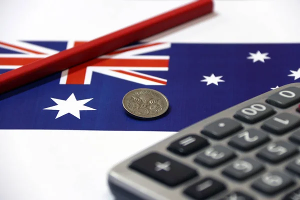 Five cents coin of Australia on the blue color of Australian nation flag with red pencil and calculator on the white floor, the concept of finance.