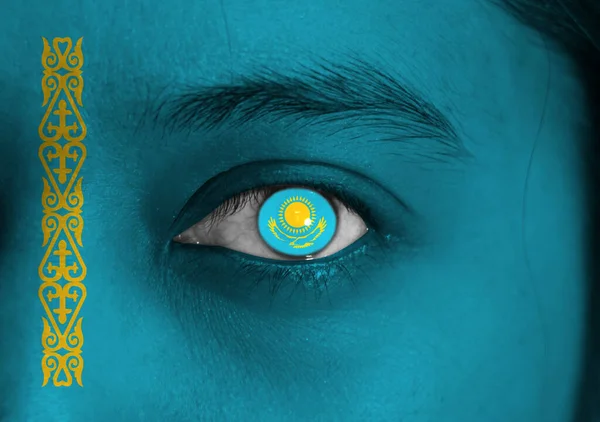 Human face painted Kazakhstan flag with a gold sun above eagle on the center of eye or eyeball. Human eye painted with flag of Kazakhstan.