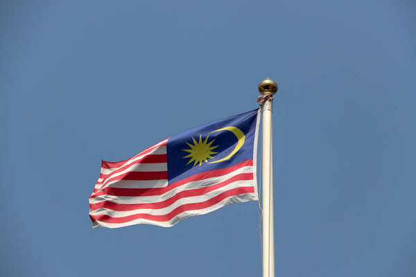 National flag of Malaysia on bright blue sky background. Blown away by wind. Malaysia is one of the ten Association of South East Asian Nations.