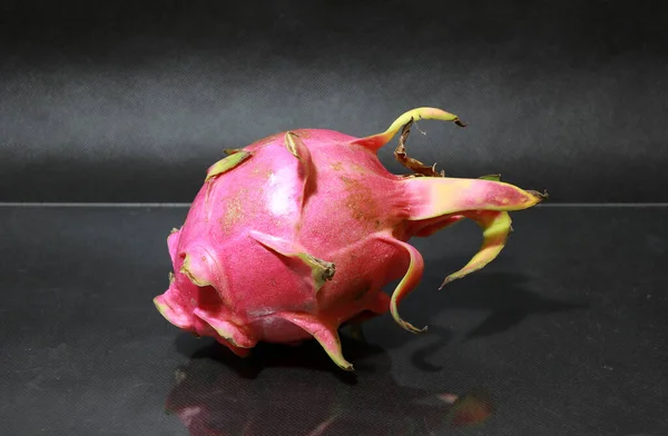 Dragon fruit on the black floor. The shape is spherical. Available in red or purple. Green cloves are attached around the fruit.