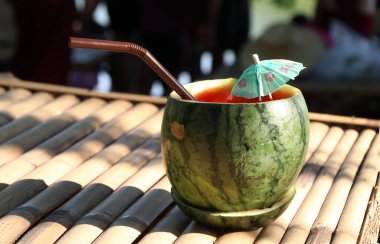 Karpuz kabında karpuz suyu ve bambu masasında küçük kağıt şemsiye. Yaz konsepti.