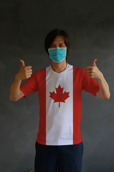 男人戴着卫生面具 双手都戴着大拇指的加拿大国旗色衬衫 加拿大保护微小灰尘或疾病的概念 — 图库照片
