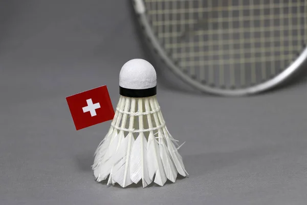 Mini Switzerland flag stick on the white shuttlecock on the grey background and out focus badminton racket. Concept of badminton sport.