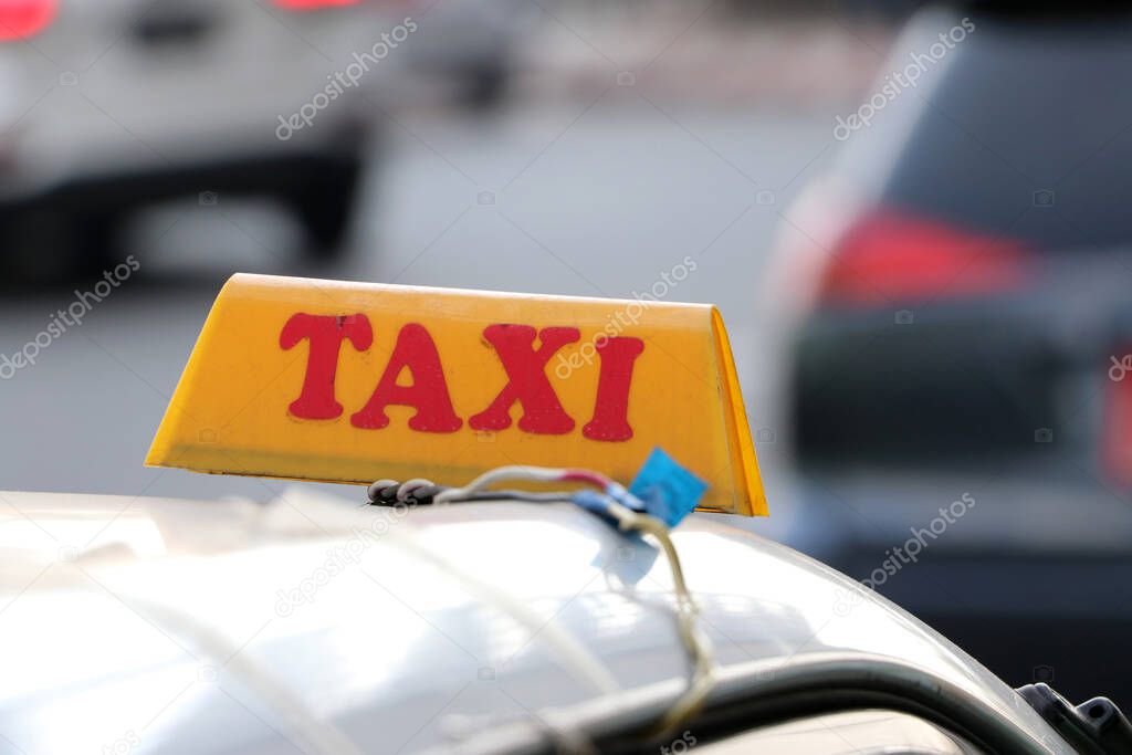 Taxi light sign or cab sign in yellow color with red text on the car roof at the street blurred background, Myanmar.