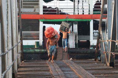 Yangon, Myanmar, 24 Şubat 2019: Myanmese işçileri büyük çantalı hindistan cevizi ve ördek yumurtalarını gemiden indirip Yangon Nehri 'ndeki liman köprüsünü yürüyerek geçiyorlar..