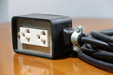 Ahşap zeminde siyah kablo olan priz. Elektrik bağlantısı için kullanılır. Elektrik ve elektrik donanımı çıkışları arasındaki uzun mesafe.