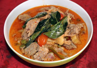 Fesleğenli tavuk, domates ve hindi üzümü kırmızı ahşap masada. Baharatlı Asyalılardan oluşan bir garnitür..