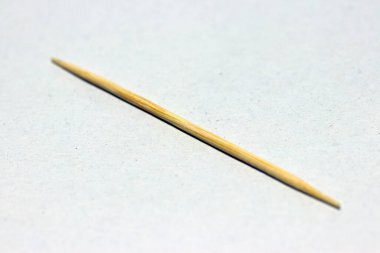 Beyaz zemine bir tahta kürdan. Dişlerin arasına sıkışmış yiyecek parçalarını çıkarmak için kullanılan kısa namlulu bir tahta parçası..