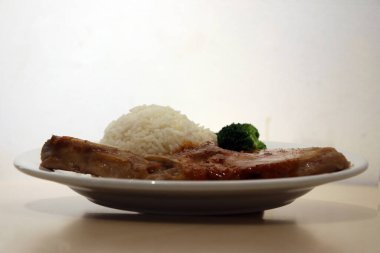 Domuz pirzolası beyaz pirinç ve ahşap masadaki tabakta yeşil brokoli. Biftek, genellikle kavurmayla veya kızartılarak pişirilen kalın dilimlere bölünmüş, hayvanın arka tarafından alınan yüksek kaliteli ettir..