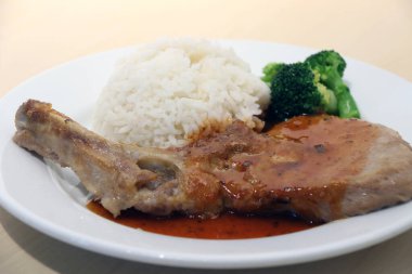 Domuz pirzolası beyaz pirinç ve ahşap masadaki tabakta yeşil brokoli. Biftek, genellikle kavurmayla veya kızartılarak pişirilen kalın dilimlere bölünmüş, hayvanın arka tarafından alınan yüksek kaliteli ettir..