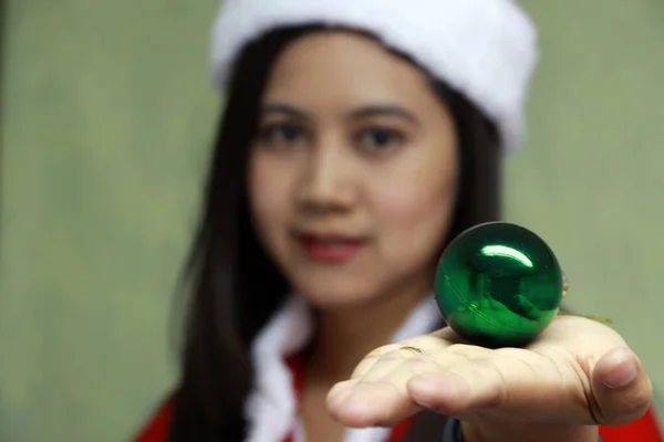 手中拿着绿色的魔球 聚焦亚洲圣诞女装 穿着红白相间的圣诞老人礼服 手里拿着绿球的女人 — 图库照片