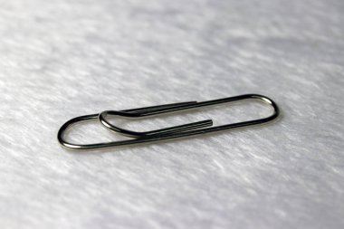 Beyaz kumaş zemine bir ataç. Birkaç kağıdı bir arada tutmak için kullanılan eğri bir tel ya da plastik parçası..