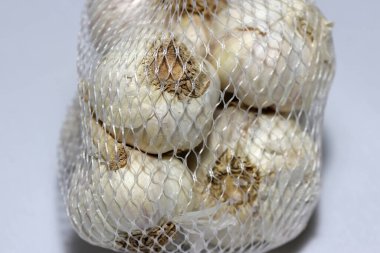 Beyaz plastik ağdaki sarımsak açık gri arka planda izole edilmiş. Sarımsak keskin kokulu bir ampuldür. Yemek ve bitkisel ilaçlarda tatlandırıcı olarak kullanılır..