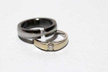 Beyaz arka planda iki elmas yüzük. Küçük dairesel bir bant, tipik olarak değerli metalden yapılmış ve genellikle bir ya da daha fazla değerli taşla sabitlenmiş, parmağına takılmış bir süs ya da evlilik, nişan ya da otorite simgesi olarak..