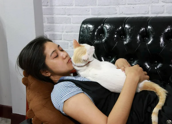 Kadın beyaz kediyle siyah kanepede uyuyor. Beyaz kedi sandalyedeki bayanın üzerine uzandı..