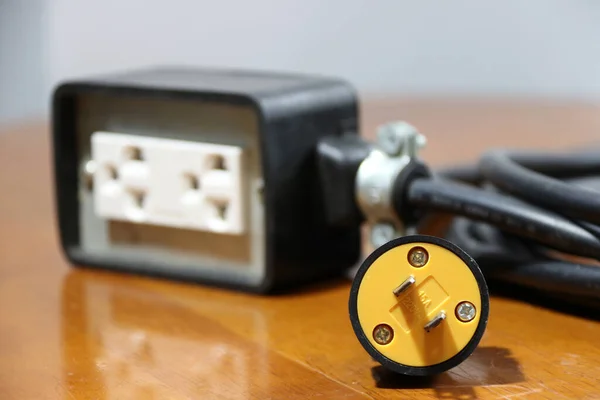 木地板上的黄色插头和带有黑色电缆的焦点出口 用于电气连接 电气设备出口之间的长距离 — 图库照片
