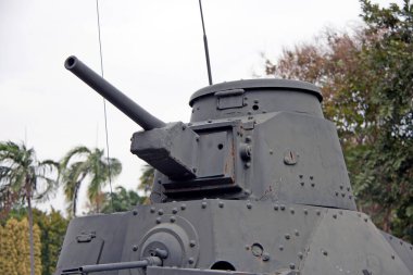 Yeşil ağaçta tank tüfeği ve beyaz gökyüzü arkaplanı. Tankın üzerinde, ağır zırhlı bir savaş aracı silah taşıyor ve sürekli eklemli metal bir yolda ilerliyor..