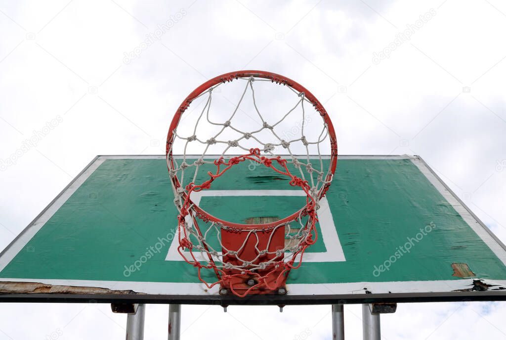 Old green board of basketball with red hoop and white-red mesh on the white sky background. basketball is a game which goals are scored by throwing a ball through a netted hoop.
