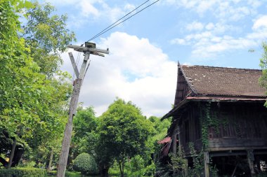 Ağaç elektrik direği ve eski geleneksel Tayland evi, mavi gökyüzü arka planındaki duvar boyunca tırmanmak..