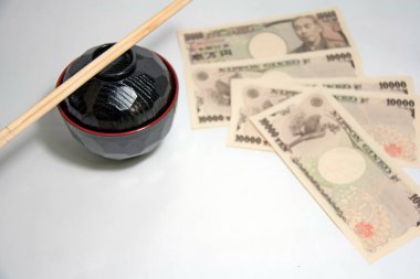 Siyah renkli, kırmızı kenarlı Miso çorba kasesi ve üzerinde Japonya 'nın Yen banknotları olan ahşap çubuklar. 