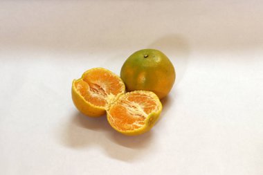 Turuncu ve soyulmuş turuncu beyaz arka planda izole edilmiş. Yuvarlak sulu bir narenciye, sert kırmızı-sarı bir kabuğu var..