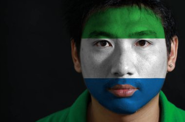 Siyah arka planda yüzünde Sierra Leone bayrağı olan bir adamın portresi açık yeşil, beyaz ve açık mavi üç renkli bir yatay renk..
