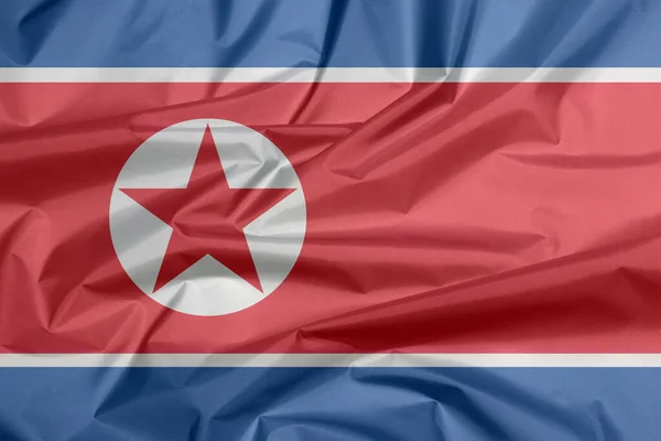 Fabric flag of North Korea. Crease of North Korean flag background, horizontal red white and blue, red star within a white circle.