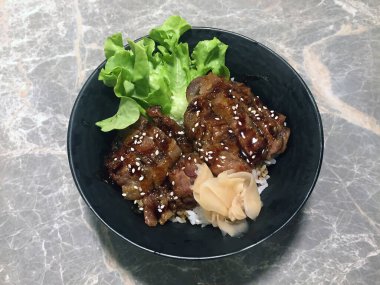 Yeşil sebzeli ızgara domuz pirinci ve turşulu zencefil, üzerine beyaz susam serpiştirilmiş. Mermer masanın üzerindeki siyah kasede..