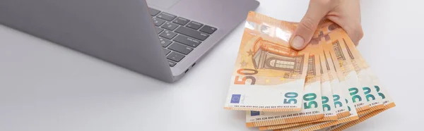 Dizüstü bilgisayarın yanında avro banknotları tutan kadın beyaz arka planda izole edilmiş, yakın görünüm