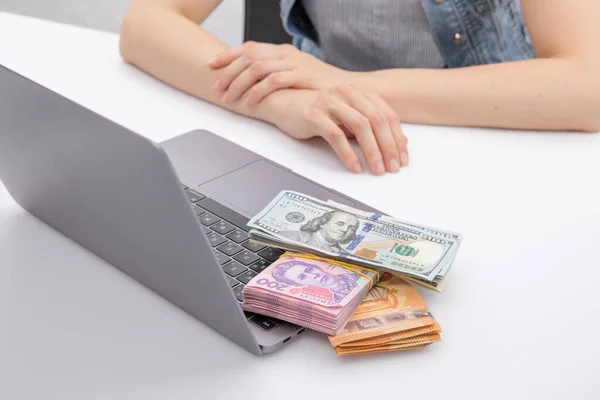 woman sitting at table near laptop with euro and dollar with hryvnia banknotes , close view