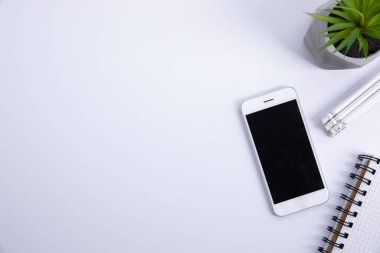 Beyaz arkaplanda izole edilmiş bitkilerle dolu kalem ve not defterli yeni modern akıllı telefon, yakın görüş 