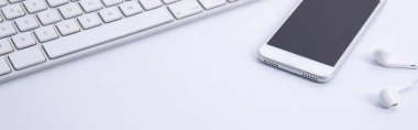 Beyaz arkaplanda izole edilmiş akıllı telefon ve kulaklıkları olan yeni modern klavye, yakın görüş 