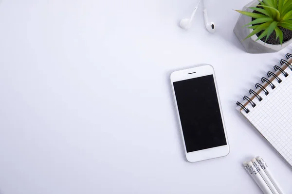 Kulaklıklı yeni modern akıllı telefon ve beyaz arka planda izole edilmiş ot bitkisi olan not defteri, yakın görüş 